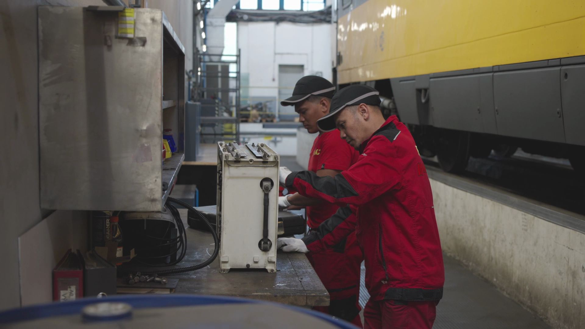 Two technicians in red RegioJet workwear working at a service unit beside a yellow train