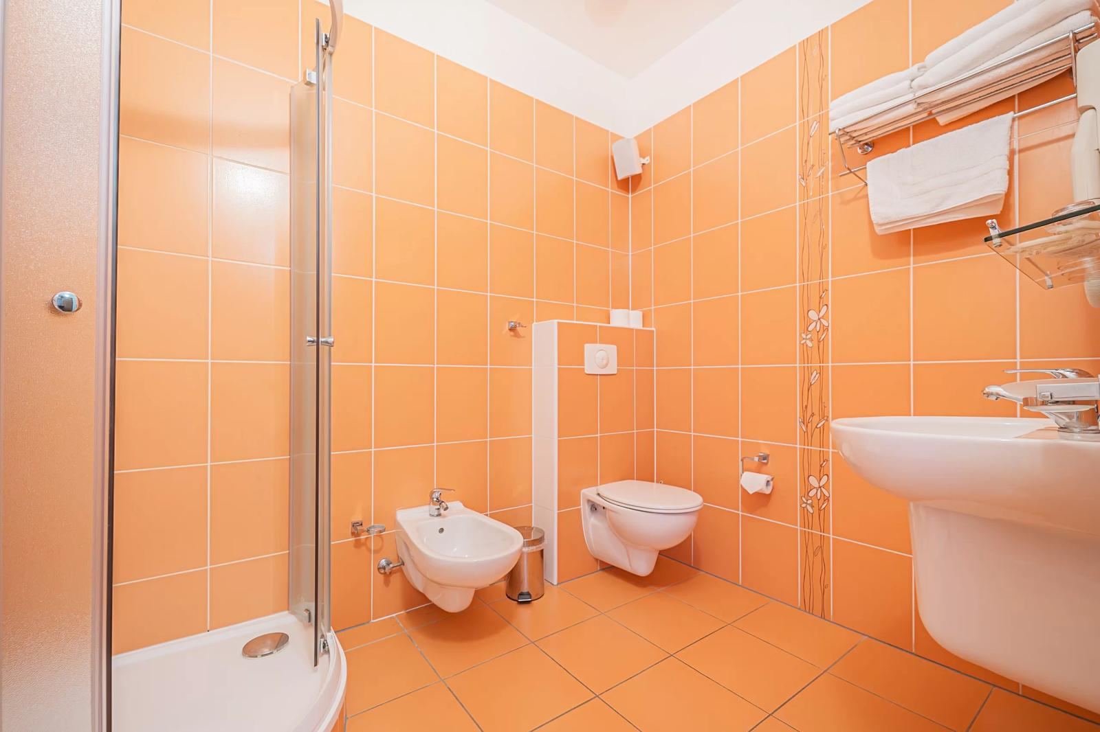 Bathroom in the accommodation with a shower, basin and warm orange tiles